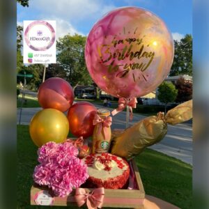 Birthday gift arrangement with pink and gold balloons, flowers, cake, and a Starbucks drink