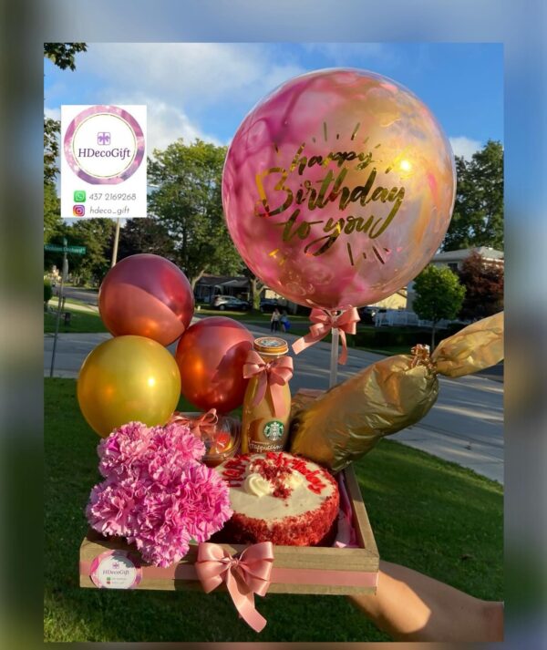 Birthday gift arrangement with pink and gold balloons, flowers, cake, and a Starbucks drink