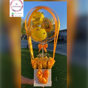 Yellow-themed welcome gift arrangement with roses and a personalized balloon reading 'Bienvenida Laura