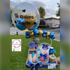 Gift basket with a large personalized balloon saying 'Te quiero Tavito' and items decorated in blue and gold