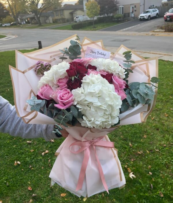 Bouquet of pink, white, and red flowers wrapped in decorative paper held outdoo