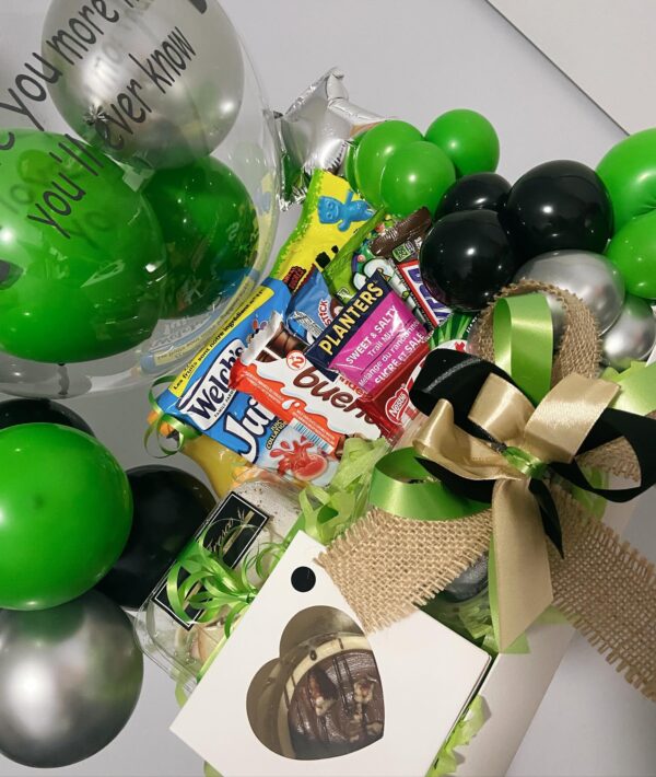 Gift basket with green, black, and silver balloons, snacks, and a gift box with a gold and black bow