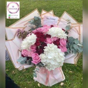 Bouquet of pink, white, and red flowers wrapped in decorative paper held outdoor