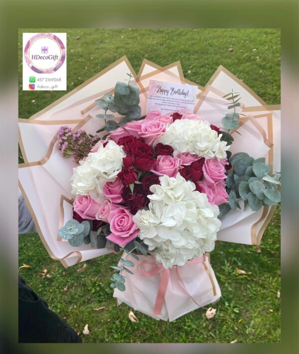 Bouquet of pink, white, and red flowers wrapped in decorative paper held outdoor